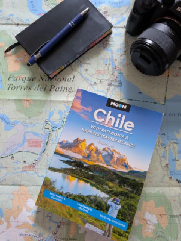 The front cover of the second edition of Moon Chile on top of a map of Torres del Paine National Park, a Sony camera and a notebook and pen